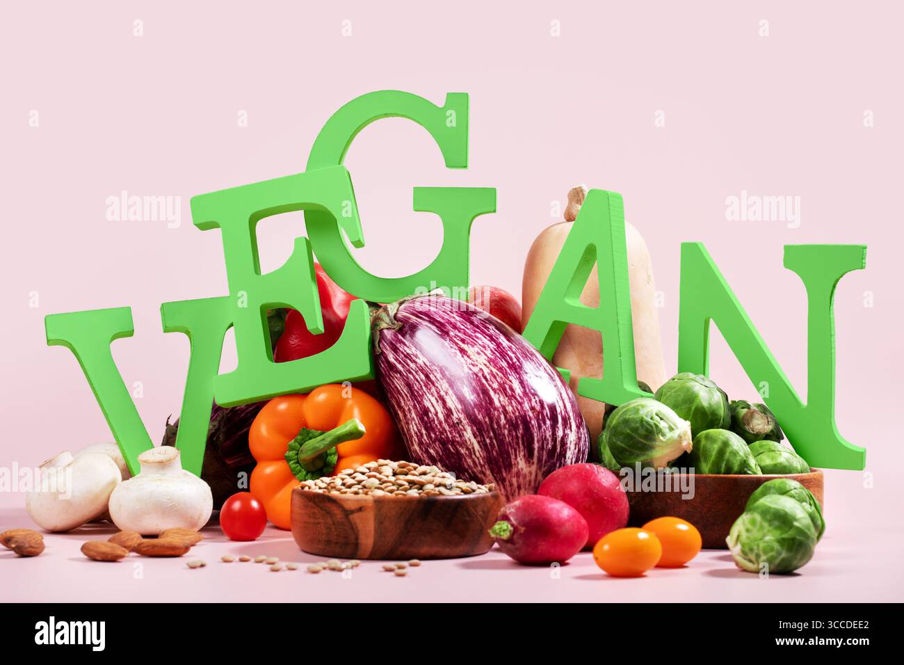 Le mot VEGAN en grandes lettres vertes sur la table rose, entouré de fruits frais, légumes et un bol de lentilles, régime végétalien nature morte Banque D'Images