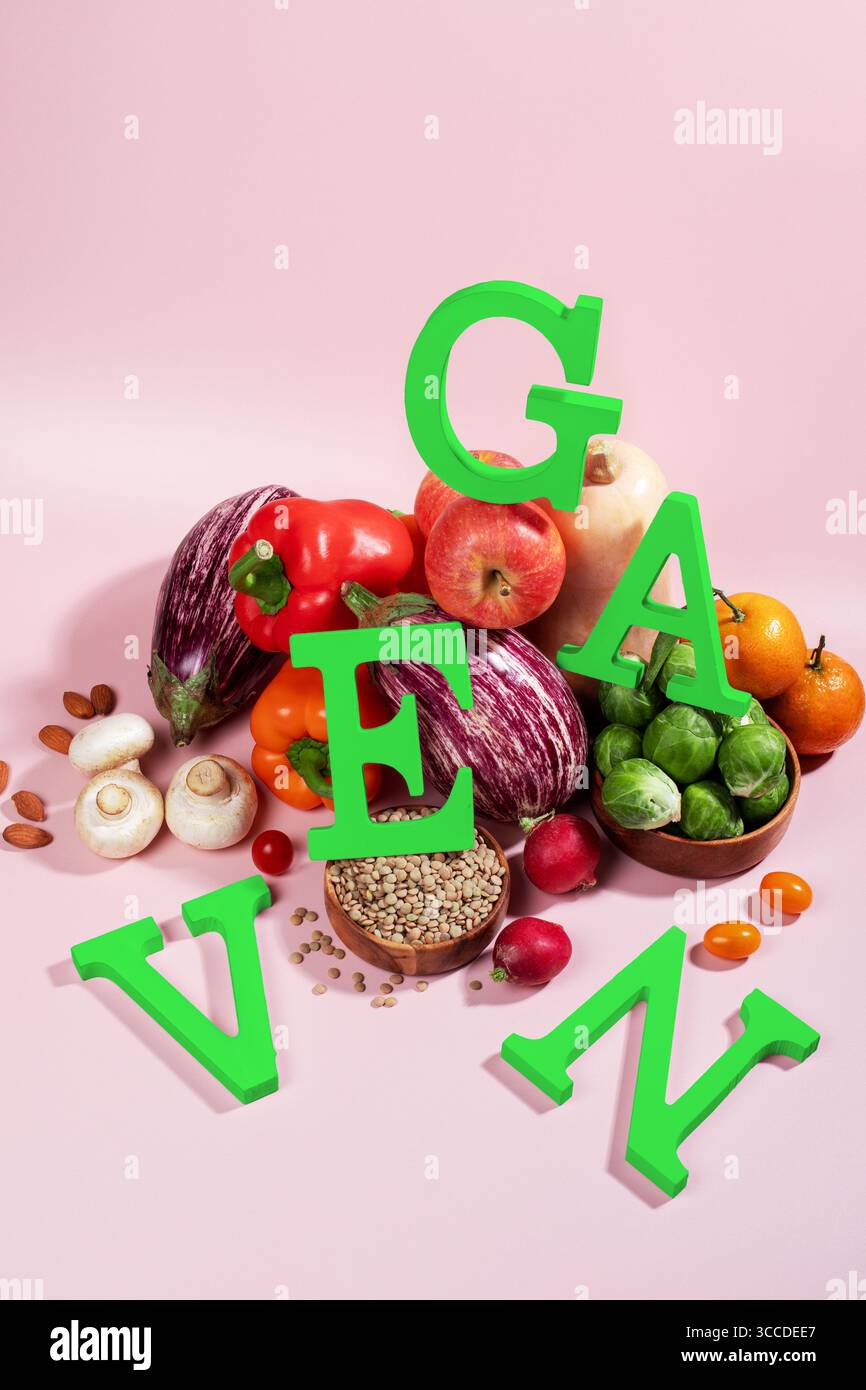 Le mot VEGAN en grandes lettres vertes sur la table rose, entouré de fruits frais, légumes et un bol de lentilles, régime végétalien nature morte Banque D'Images