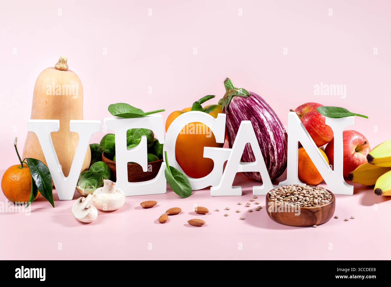 Le mot VEGAN en grandes lettres sur la table rose, entouré de fruits frais, légumes et un bol de lentilles, régime végétalien nature morte Banque D'Images