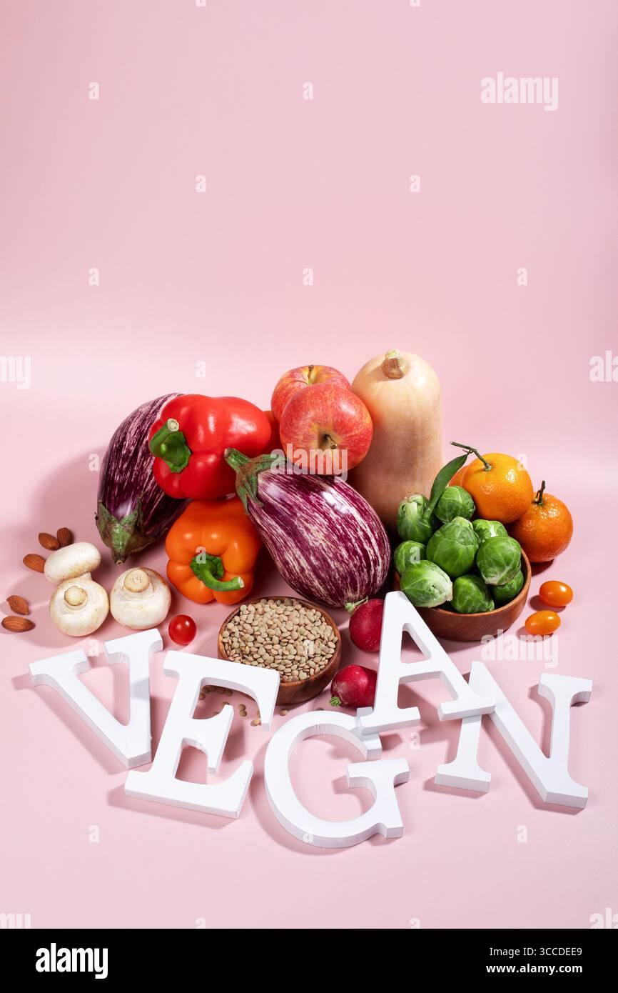Le mot VEGAN en grandes lettres sur la table rose, entouré de fruits frais, légumes et un bol de lentilles, régime végétalien nature morte Banque D'Images