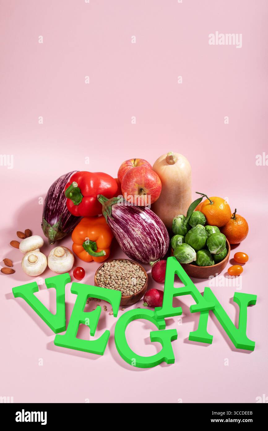 Le mot VEGAN en grandes lettres vertes sur la table rose, entouré de fruits frais, légumes et un bol de lentilles, régime végétalien nature morte Banque D'Images