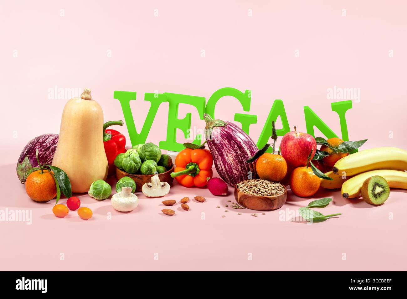 Le mot VEGAN en grandes lettres vertes sur la table rose, entouré de fruits frais, légumes et un bol de lentilles, régime végétalien nature morte Banque D'Images