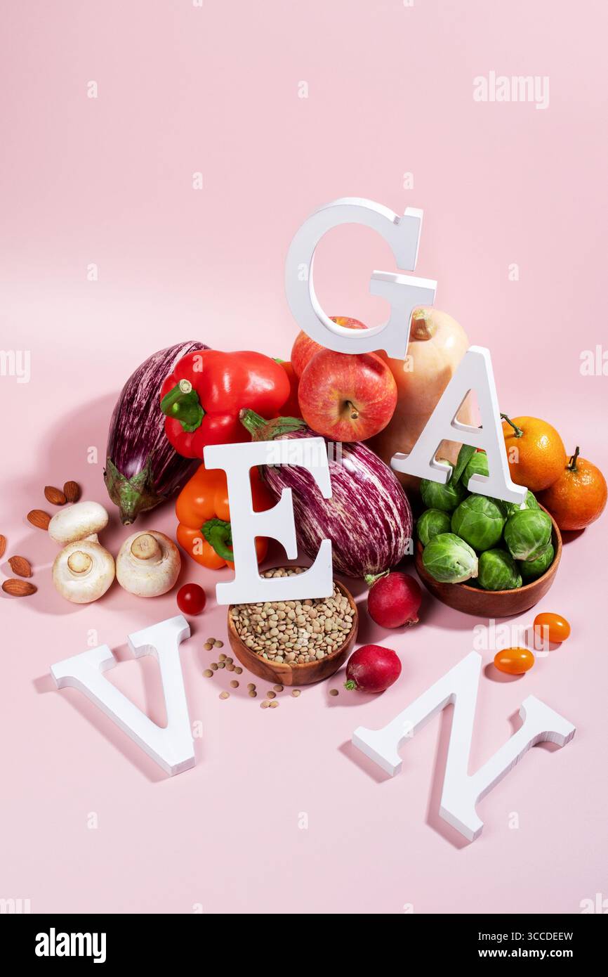 Le mot VEGAN en grandes lettres sur la table rose, entouré de fruits frais, légumes et un bol de lentilles, régime végétalien nature morte Banque D'Images