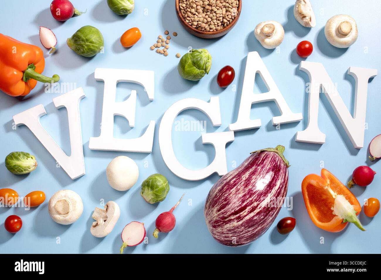 Le mot VEGAN en grandes lettres blanches sur une surface bleue, entouré de fruits frais, de légumes et d'un bol de lentilles, vegan Diet Flat lay Banque D'Images
