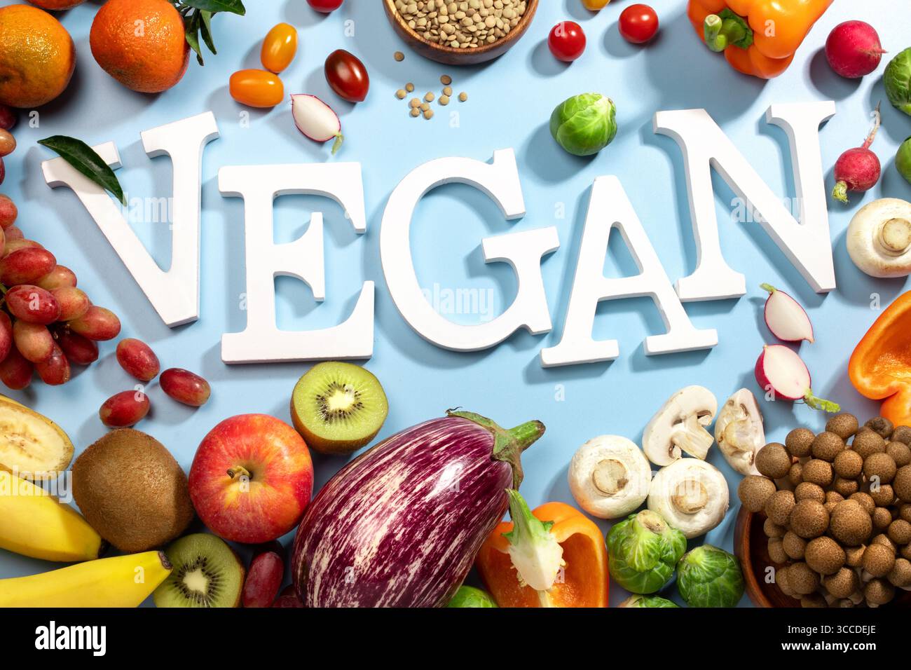 Le mot VEGAN en grandes lettres blanches sur une surface bleue, entouré de fruits frais, de légumes et d'un bol de lentilles, vegan Diet Flat lay Banque D'Images