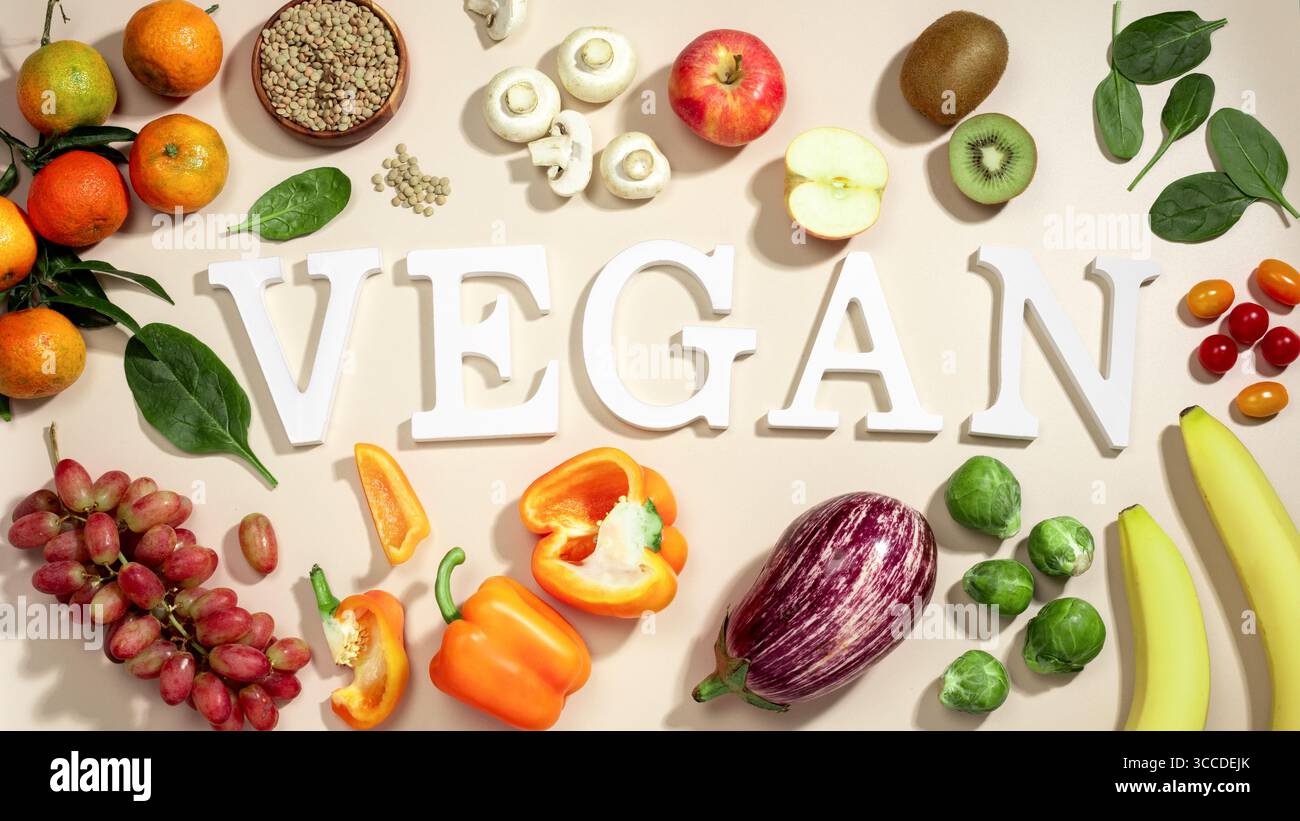 Le mot VEGAN en grandes lettres sur la table beige, entouré de fruits frais, de légumes et d'un bol de lentilles, végétalien régime plat posé Banque D'Images