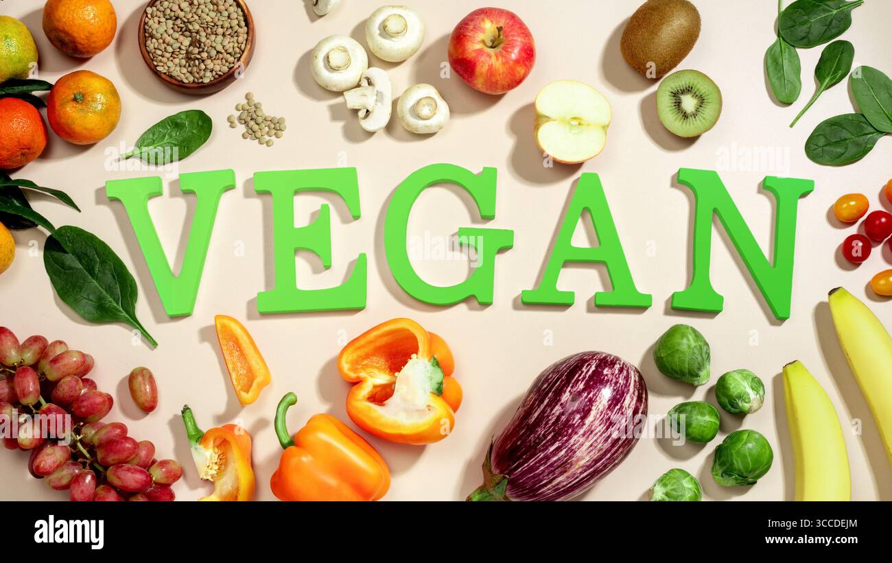 Le mot VEGAN en grandes lettres vertes sur la table beige, entouré de fruits frais, légumes et un bol de lentilles, végétalien plat de régime Banque D'Images