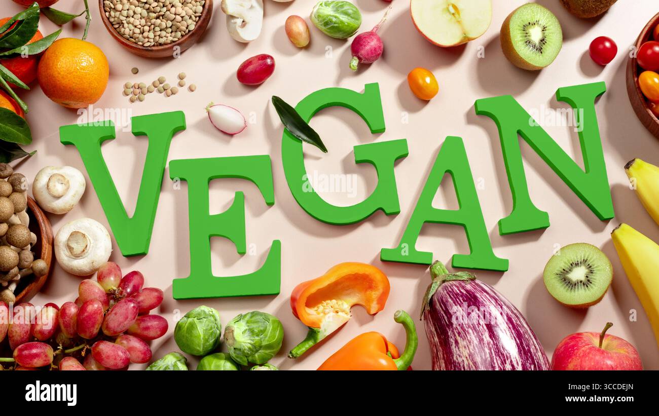 Le mot VEGAN en grandes lettres vertes sur la table beige, entouré de fruits frais, légumes et un bol de lentilles, végétalien plat de régime Banque D'Images