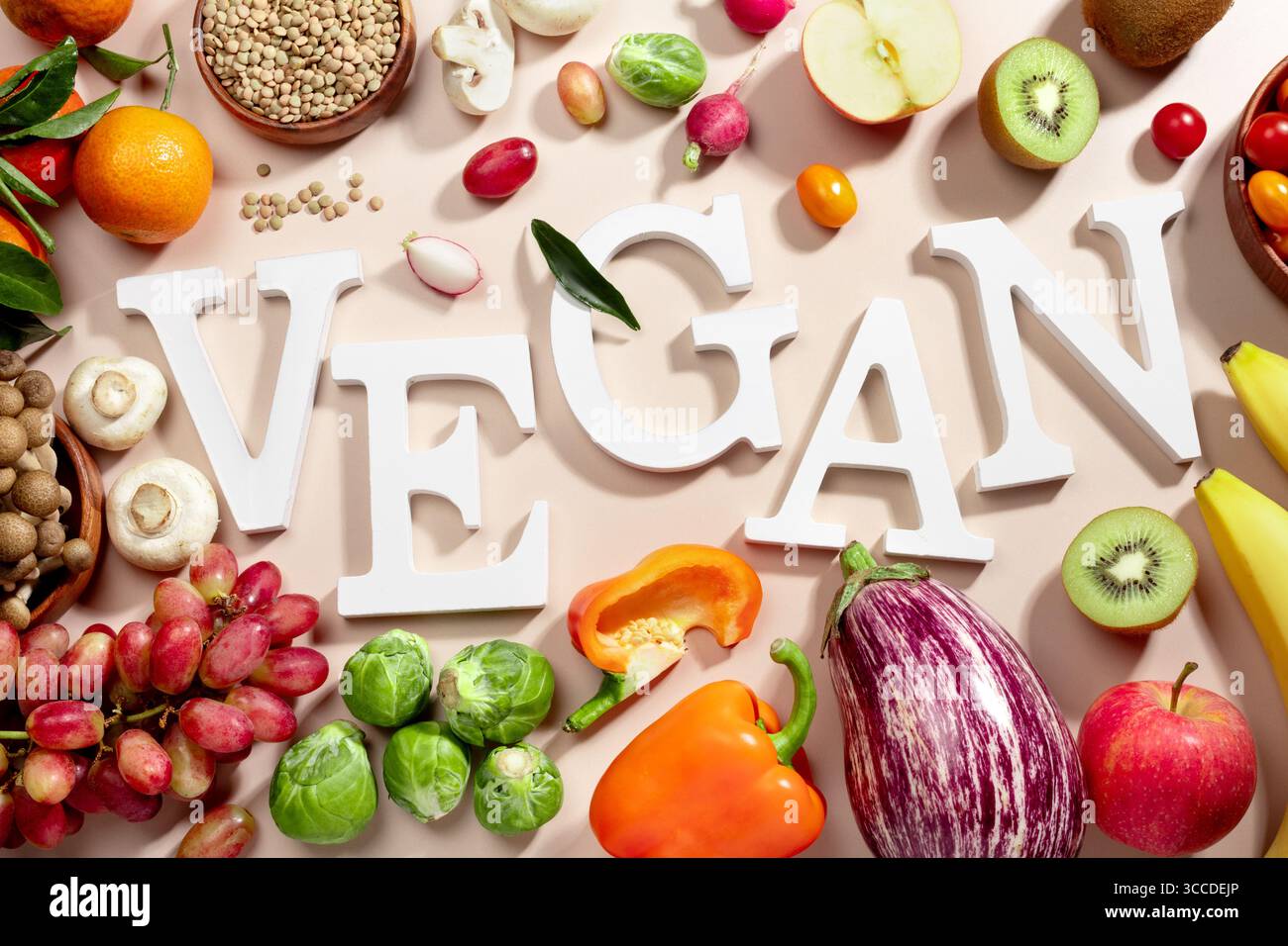 Le mot VEGAN en grandes lettres sur la table beige, entouré de fruits frais, de légumes et d'un bol de lentilles, végétalien régime plat posé Banque D'Images