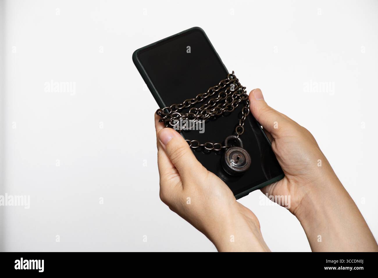 Mains féminines tenant un smartphone enveloppé dans une chaîne métallique avec un cadenas sur fond blanc sur le thème de la sécurité des mots de passe et des données Banque D'Images