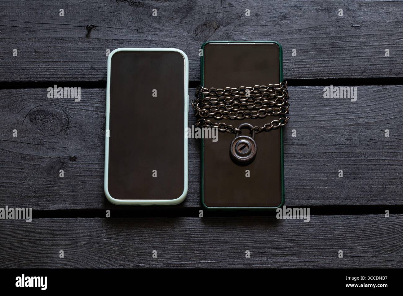Deux smartphones sur une surface en bois noir, l'un enveloppé d'une chaîne métallique avec un cadenas, l'autre sans cadenas sur le thème de la sécurité et des données p Banque D'Images
