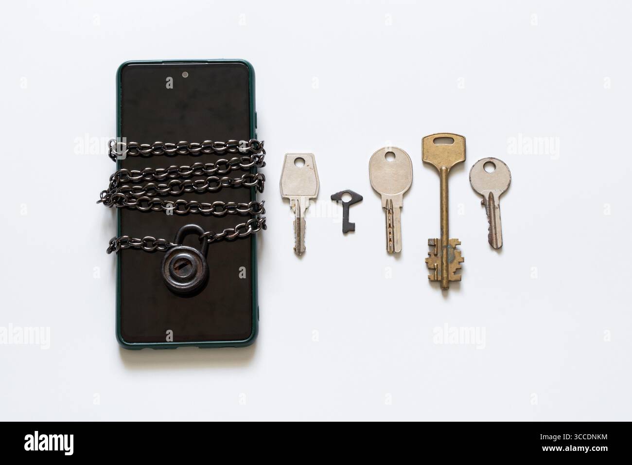 Smartphone dans un étui vert enveloppé dans une chaîne en métal avec serrure et cinq clés différentes couchées à proximité sur fond blanc gros plan Banque D'Images