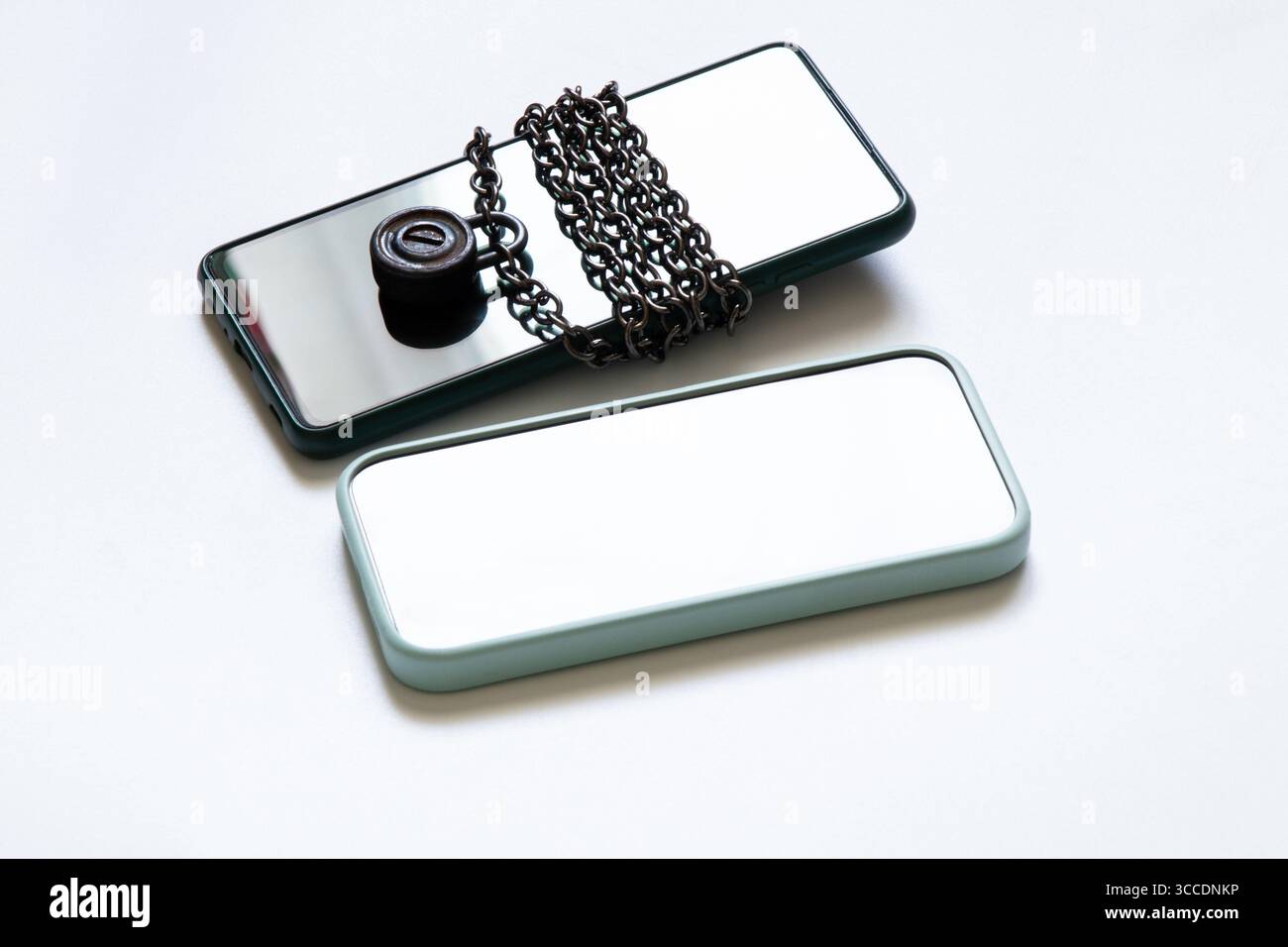 Deux smartphones sont couchés sur un fond blanc et l'un est enveloppé d'une chaîne en métal avec un verrou, l'autre est sans verrou sur le sujet de la securit Banque D'Images