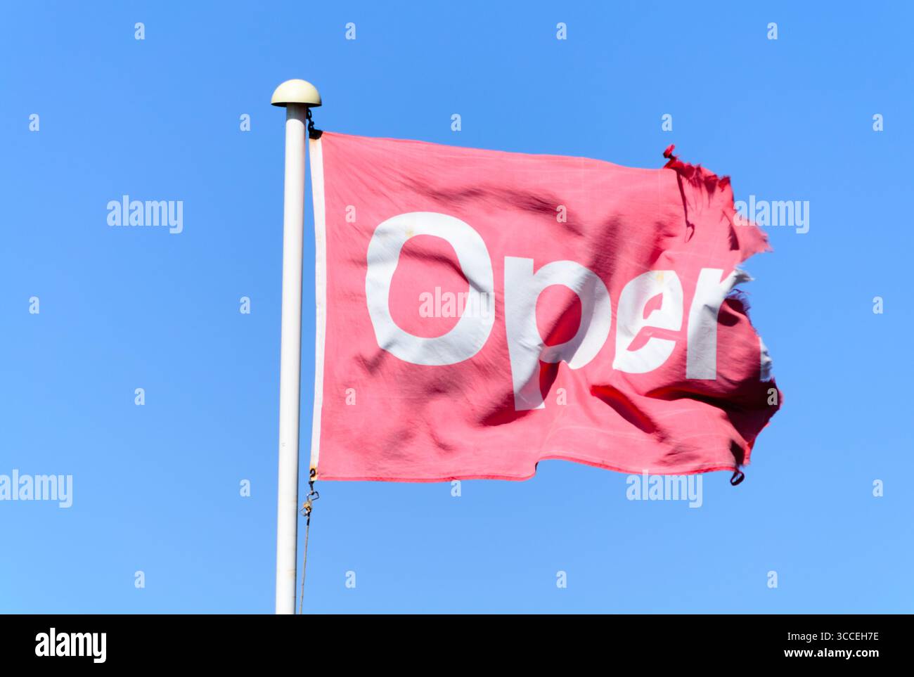 Un drapeau rouge sur un mât de drapeau disant ouvert sur un fond de ciel bleu UK Banque D'Images