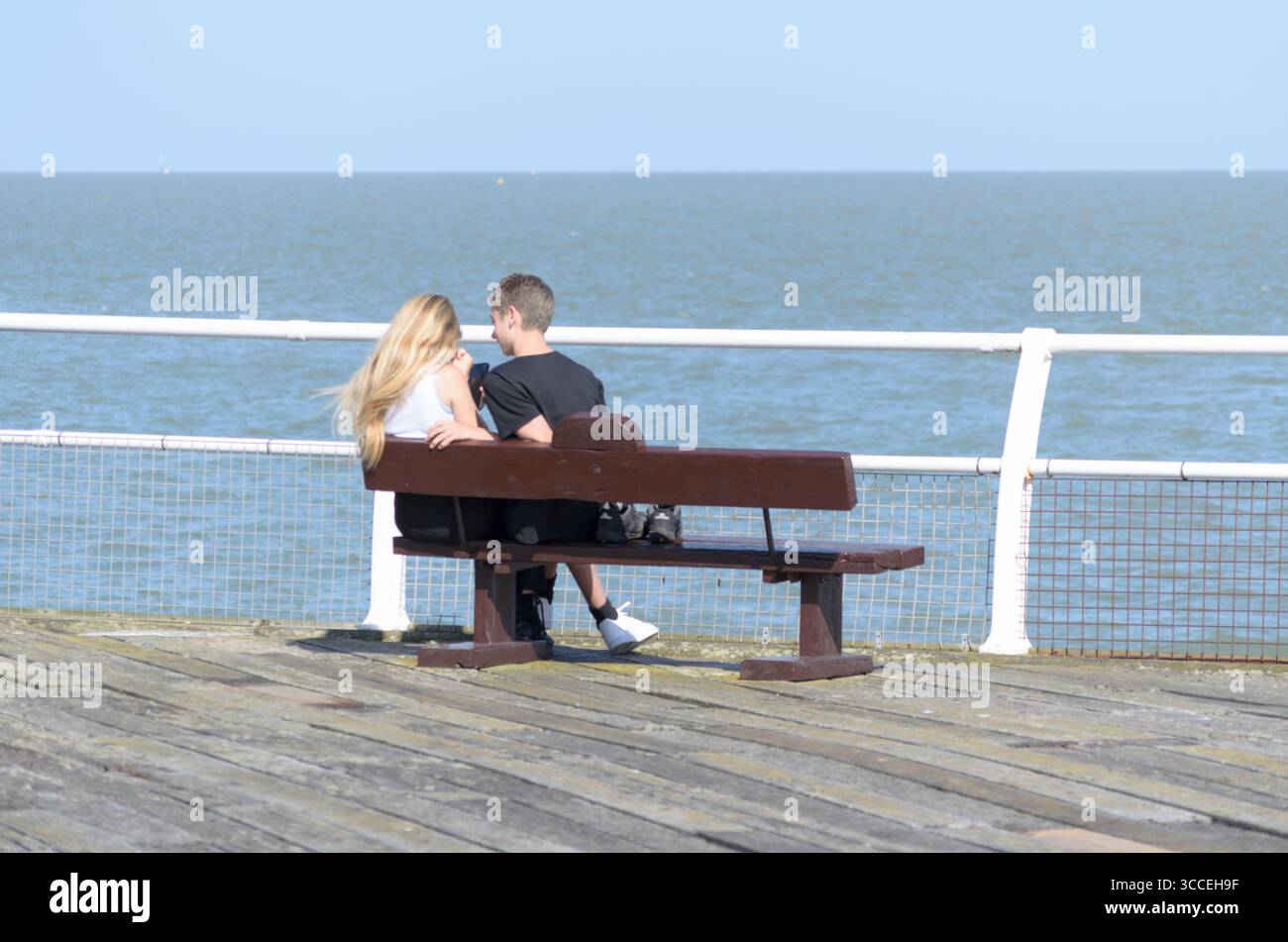Jeune couple assis sur un banc donnant sur la mer au bout de la jetée UK Banque D'Images