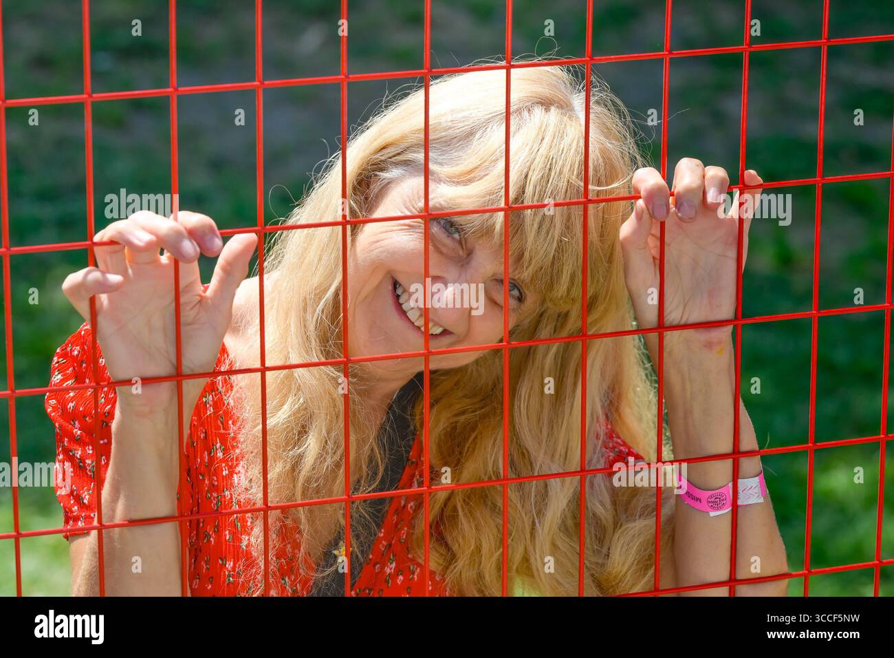 femme aux cheveux blonds souriant à travers une clôture de fil rouge Banque D'Images