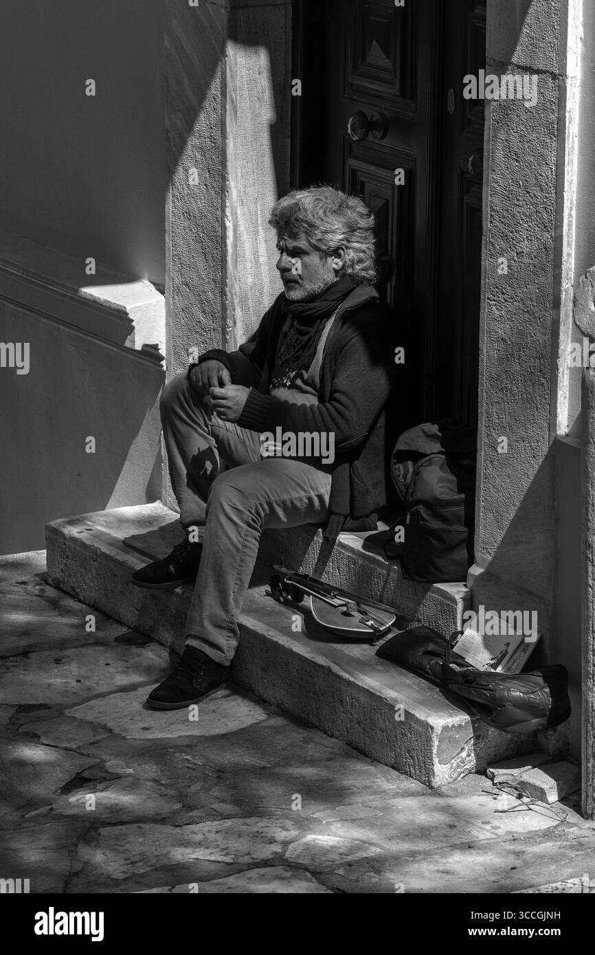 Un busker joue d'un instrument traditionnel dans une porte à Athènes, en Grèce, par une chaude journée de juillet, remplissant la rue ensoleillée de musique et d'énergie urbaine. Banque D'Images