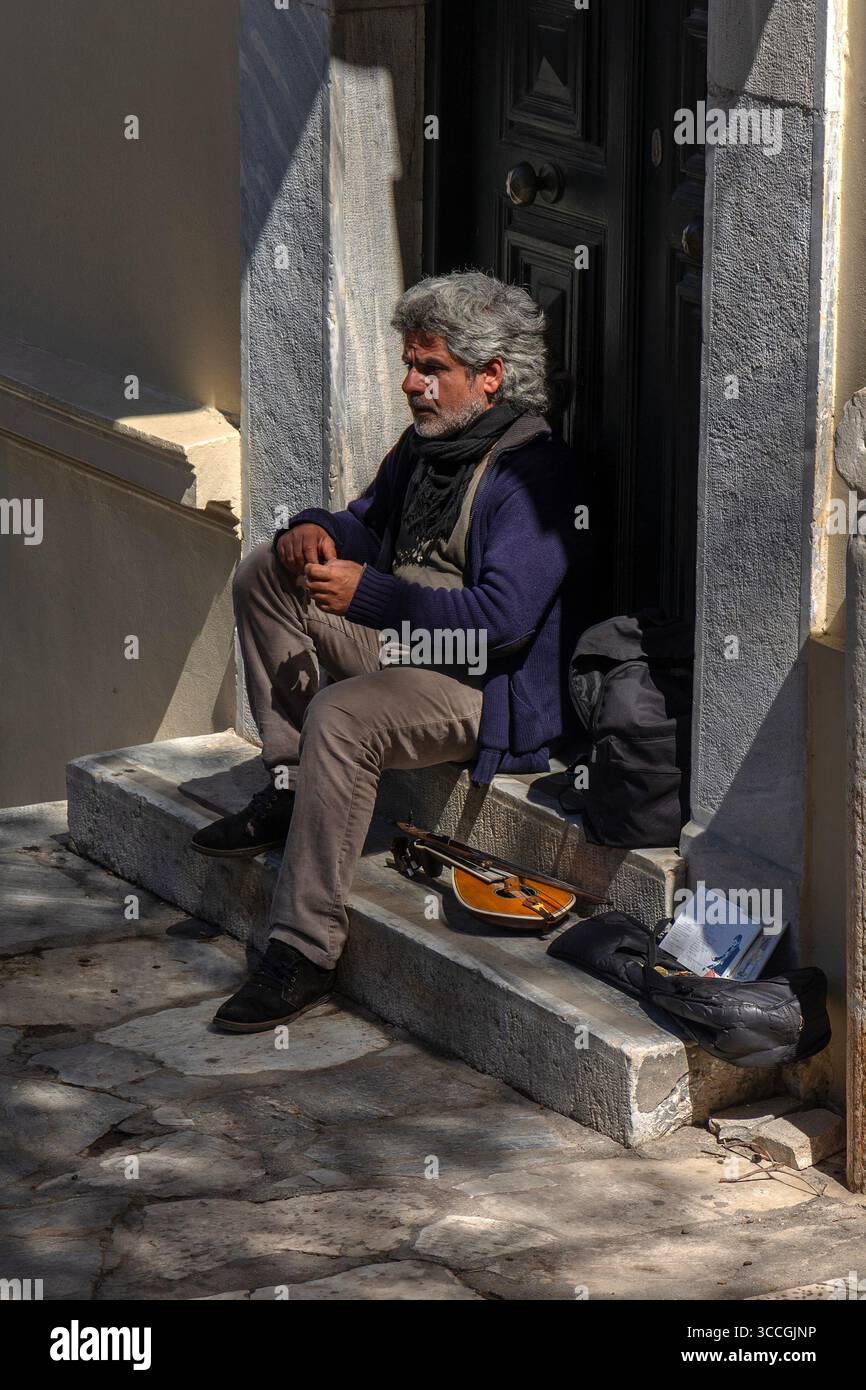 Un busker joue d'un instrument traditionnel dans une porte à Athènes, en Grèce, par une chaude journée de juillet, remplissant la rue ensoleillée de musique et d'énergie urbaine. Banque D'Images