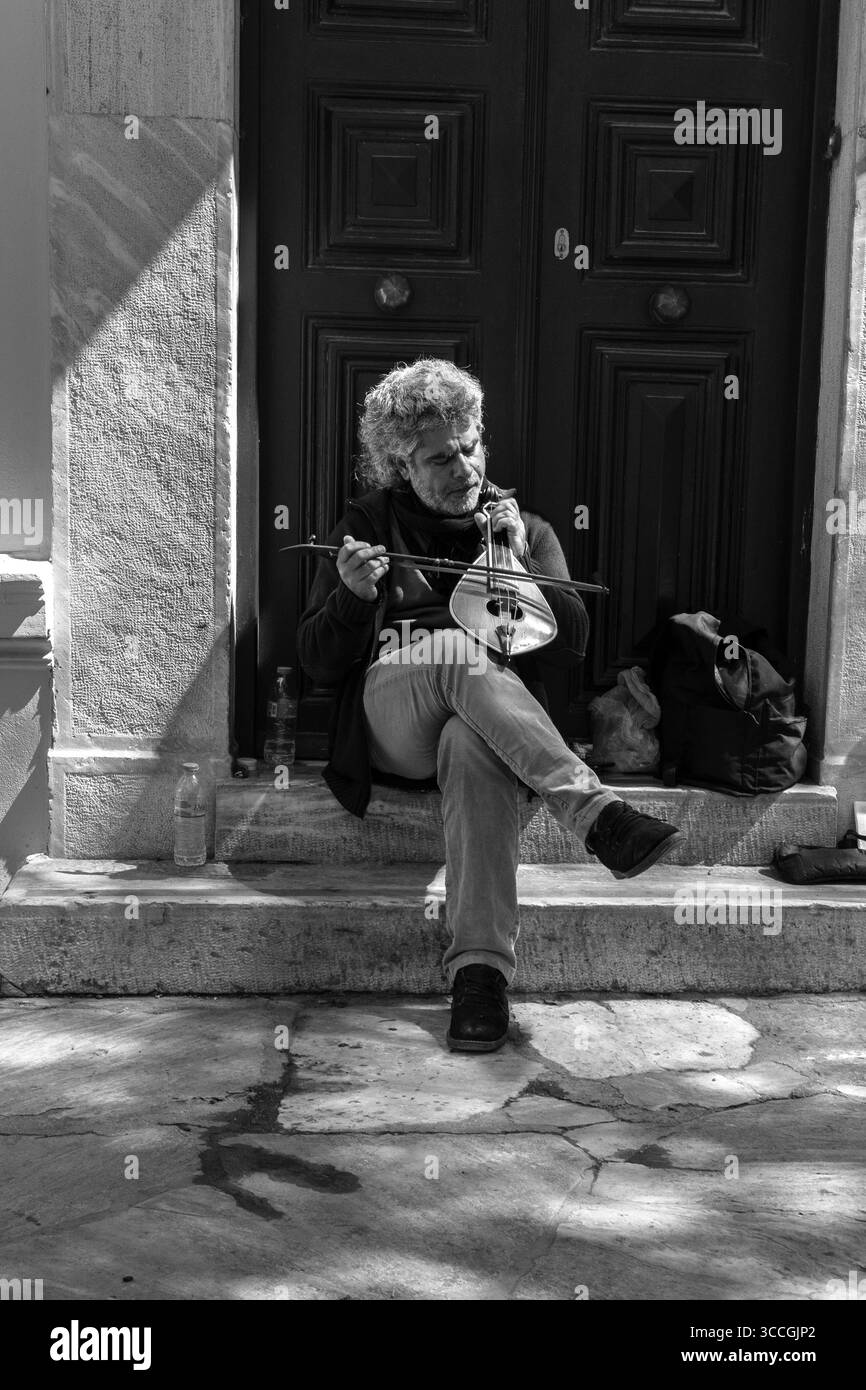 Un busker joue d'un instrument traditionnel dans une porte à Athènes, en Grèce, par une chaude journée de juillet, remplissant la rue ensoleillée de musique et d'énergie urbaine. Banque D'Images