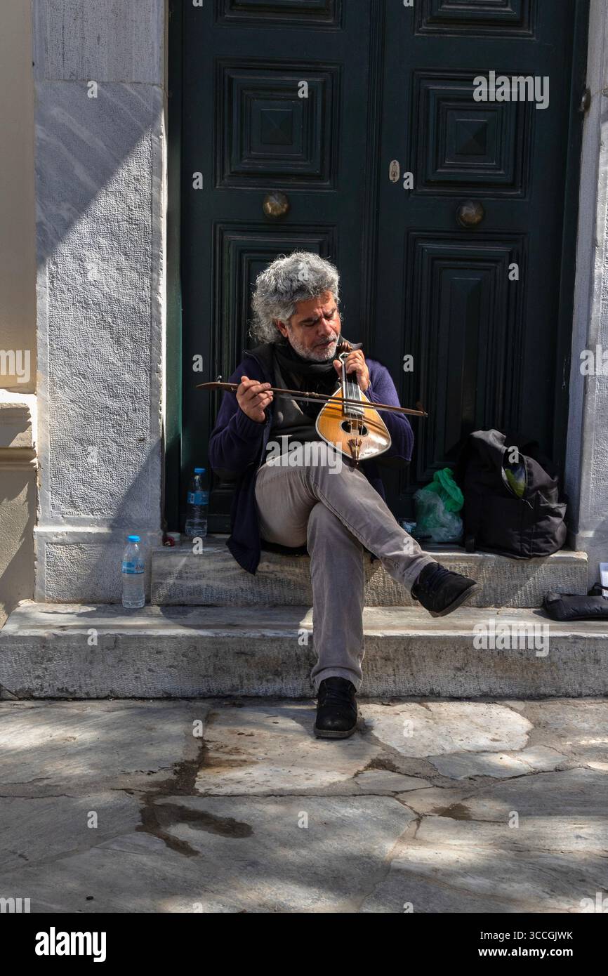 Un busker joue d'un instrument traditionnel dans une porte à Athènes, en Grèce, par une chaude journée de juillet, remplissant la rue ensoleillée de musique et d'énergie urbaine. Banque D'Images