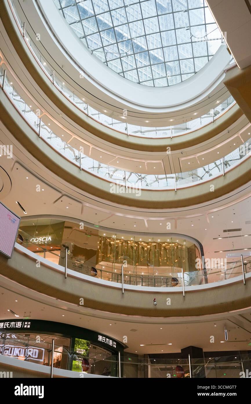 À l'intérieur d'un centre commercial, les escaliers roulent sous de hauts plafonds tandis que les clients passent devant des vitrines lumineuses, avec des reflets façonnant une scène moderne. Hongkou Dist Banque D'Images