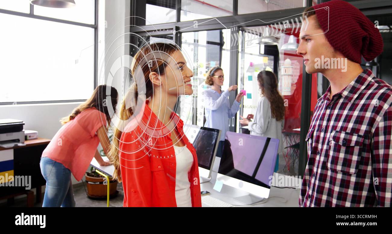 Discuter des collègues portant une chemise rouge près des ordinateurs dans un bureau ouvert, des notes adhésives colorées Banque D'Images