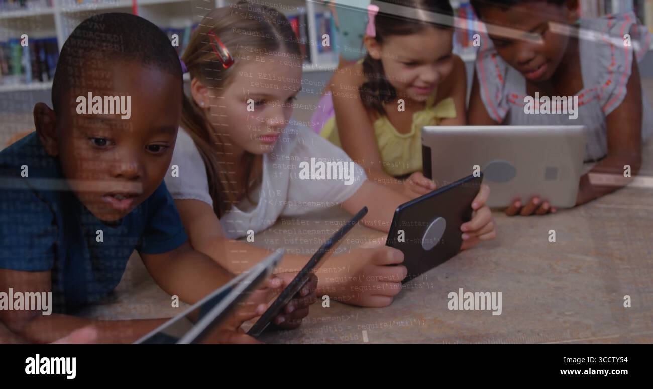 Groupe couché de quatre enfants utilisant des tablettes à écran tactile sur le sol de la bibliothèque en bois, avec des étagères Banque D'Images