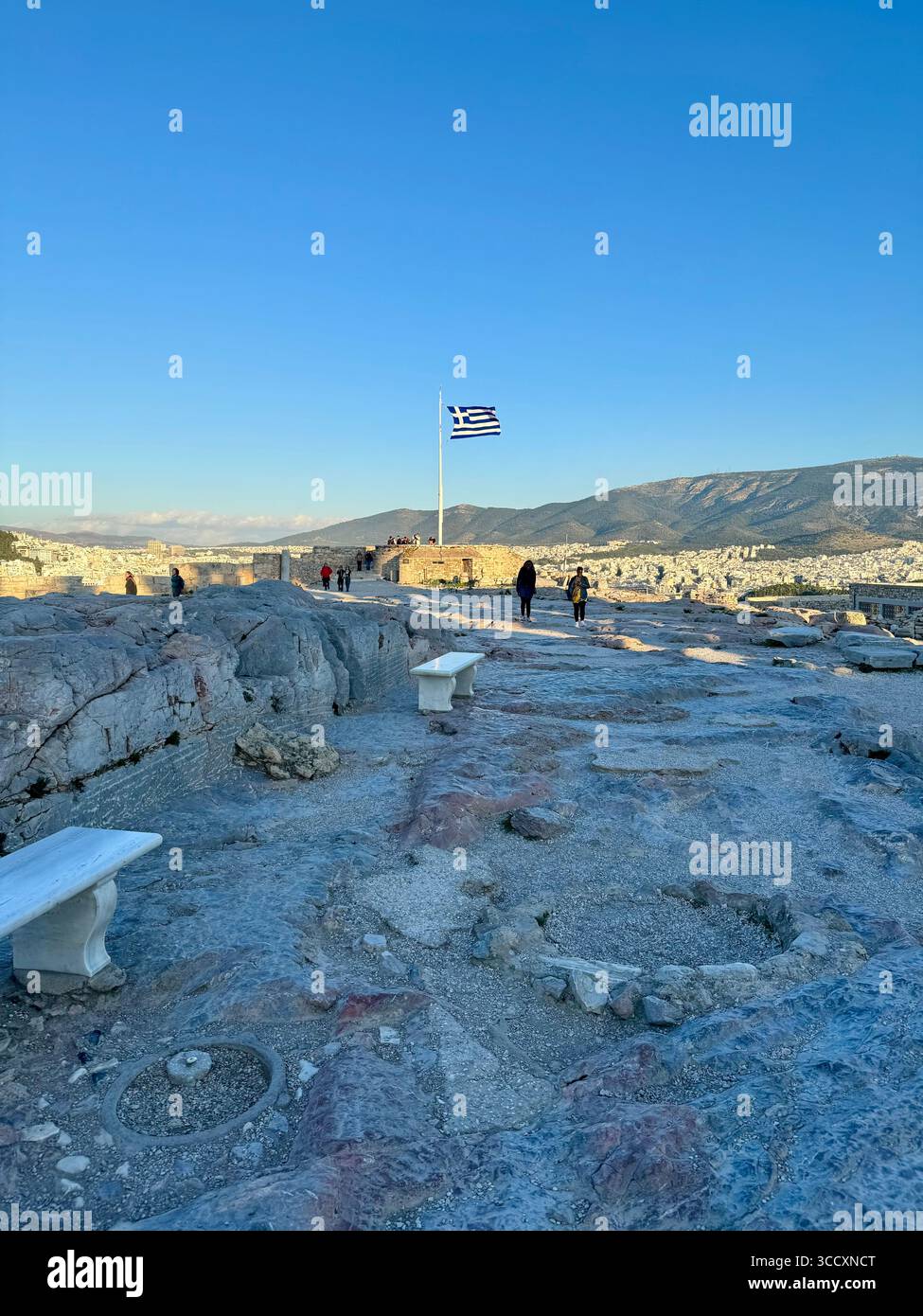 Le drapeau grec flotte fièrement au monument du drapeau au sommet de l'Acropole à Athènes, en Grèce, offrant une vue panoramique sur la ville. Banque D'Images