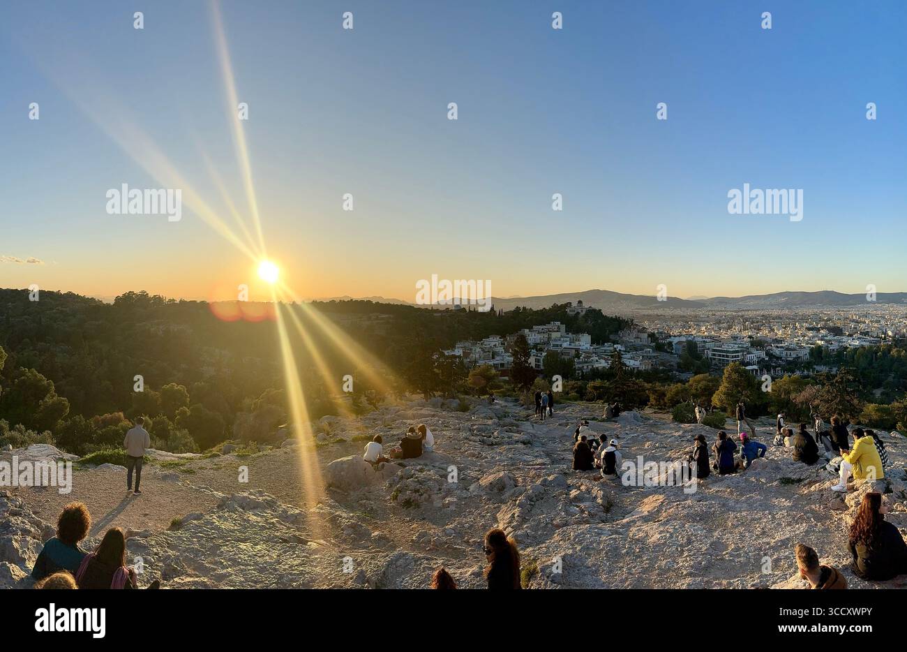 Coucher de soleil pendant l'heure dorée à la colline d'Areopagus avec des gens rassemblés pour regarder le paysage urbain d'Athènes. Banque D'Images