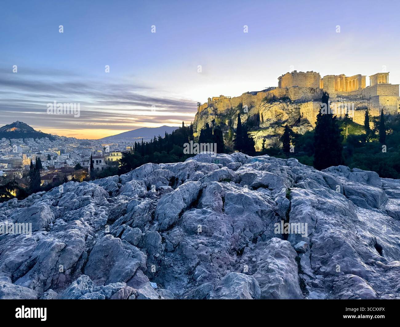Lever de soleil sur la colline d'Areopagus avec la lumière chaude du matin illuminant l'Acropole et le paysage urbain d'Athènes. Banque D'Images