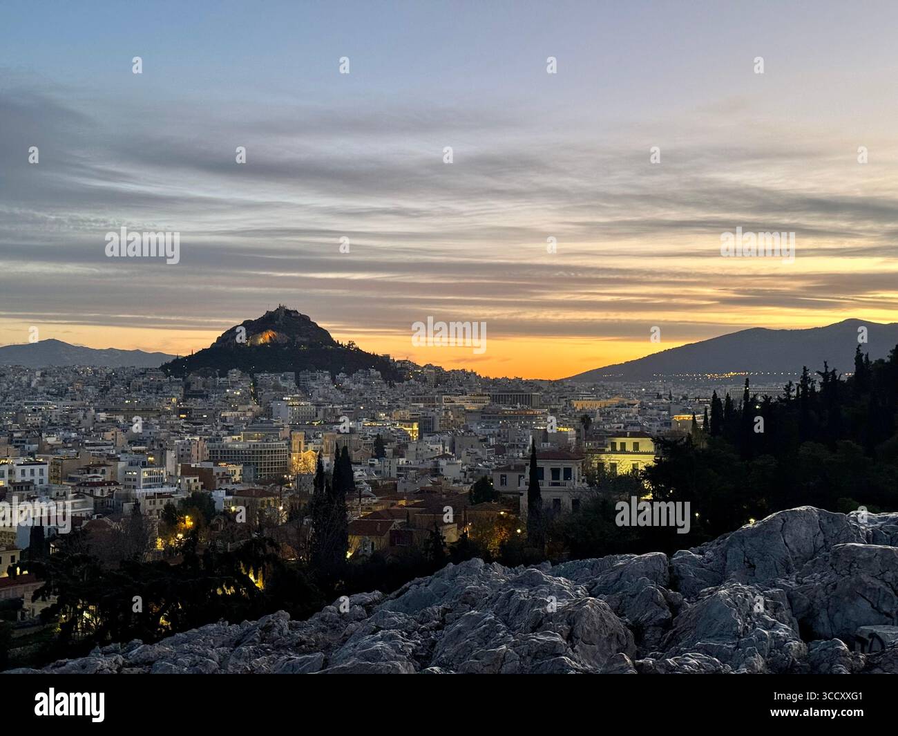 Lever de soleil sur Athènes vu de la colline d'Areopagus avec la colline illuminée de Lycabette visible au loin sous un ciel nuageux en couches. - Image de stock capturée avec un smartphone