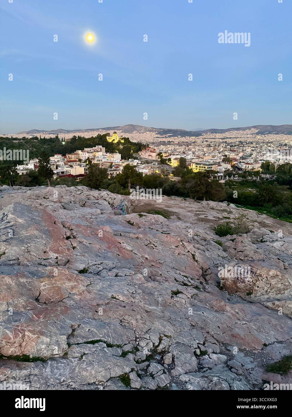 Vue du lever du soleil depuis la colline d'Areopagus avec le paysage urbain d'Athènes, mettant en valeur le bâtiment jaune et la montagne lointaine. - Image de stock capturée avec un smartphone