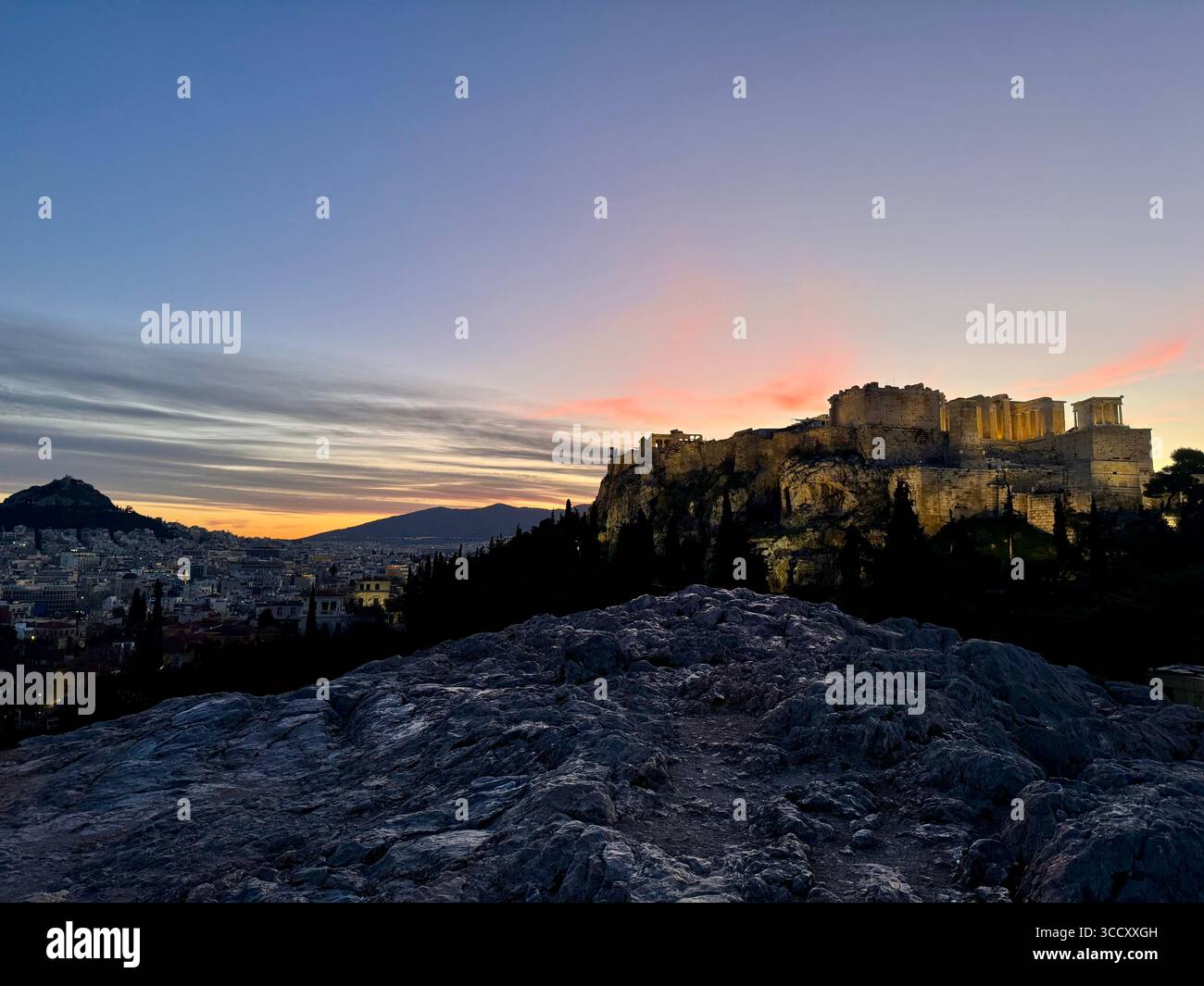 Lever de soleil sur la colline d'Areopagus avec la lumière chaude du matin illuminant l'Acropole et le paysage urbain d'Athènes. Banque D'Images