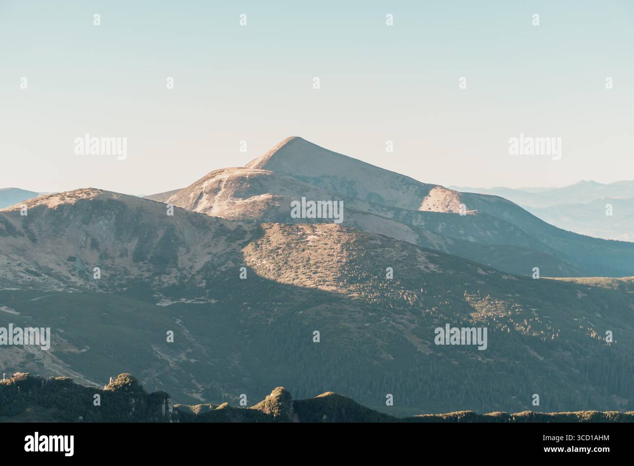 Sommet montagneux s'élevant au-dessus de crêtes superposées sous un ciel pastel clair avec une douce lumière automnale projetant de douces ombres sur les pentes des hautes terres sereines Banque D'Images
