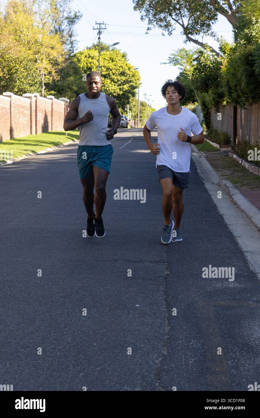 Divers amis masculins courir sur la route de banlieue portant des chaussures de course vérifiant le rythme sur les montres de sport Banque D'Images