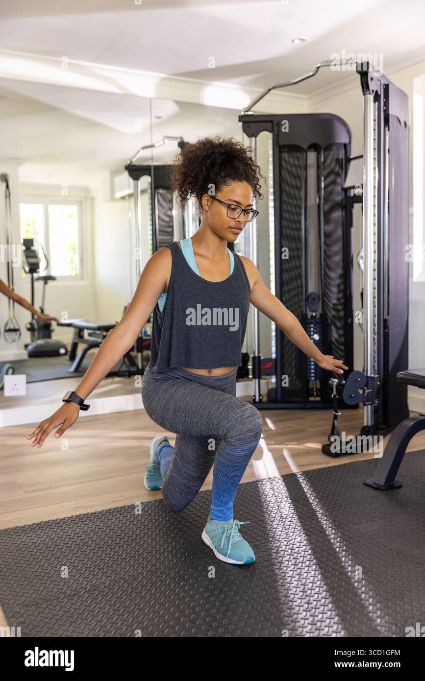 Femme afro-américaine en vêtements de sport effectuant des fentes sur tapis en caoutchouc dans la salle de gym à domicile avec machine à câble Banque D'Images