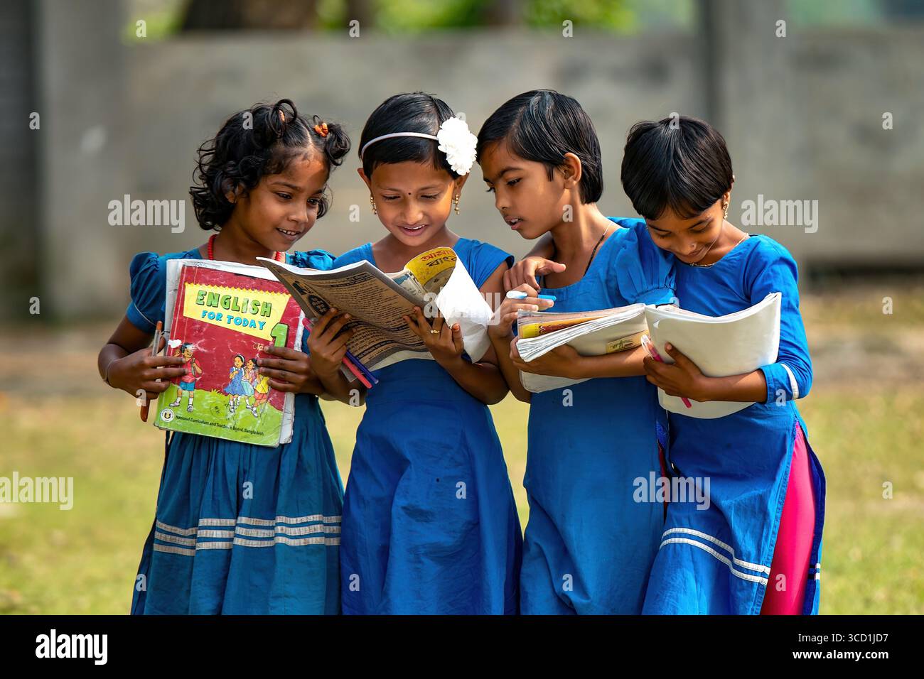 Bogura, Bangladesh - 13 décembre 2019 : vue d'élèves enthousiastes en uniforme bleu vif se blottissent ensemble, les yeux fixés sur des manuels et des cahiers, baignés dans la douce lumière du jour d'une cour d'école. Banque D'Images