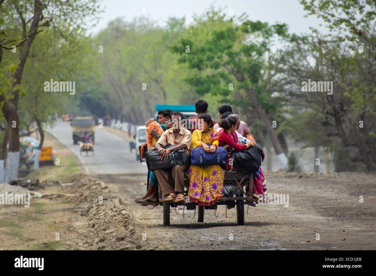 Bogura, Bangladesh - 07 avril 2018 : vue d'un groupe dynamique de personnes entassées sur un chariot rustique, leurs vêtements colorés contrastent fortement avec la route poussiéreuse. Banque D'Images