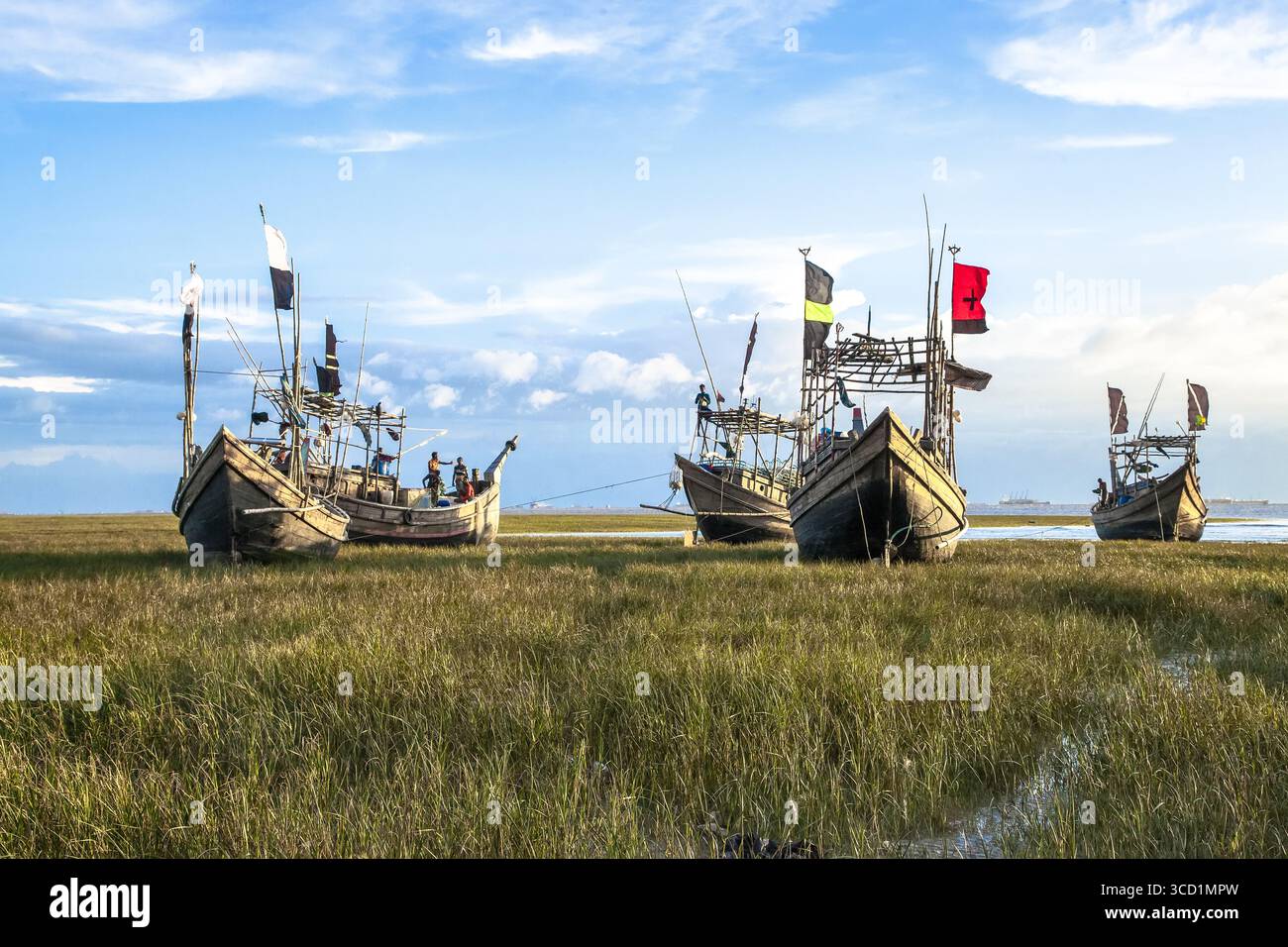 Chattogram, Bangladesh - 19 septembre 2023 : vue de bateaux de pêche reposant sur la côte herbeuse, leurs drapeaux colorés flottant doucement dans la brise sous un ciel vaste et nuageux. Banque D'Images