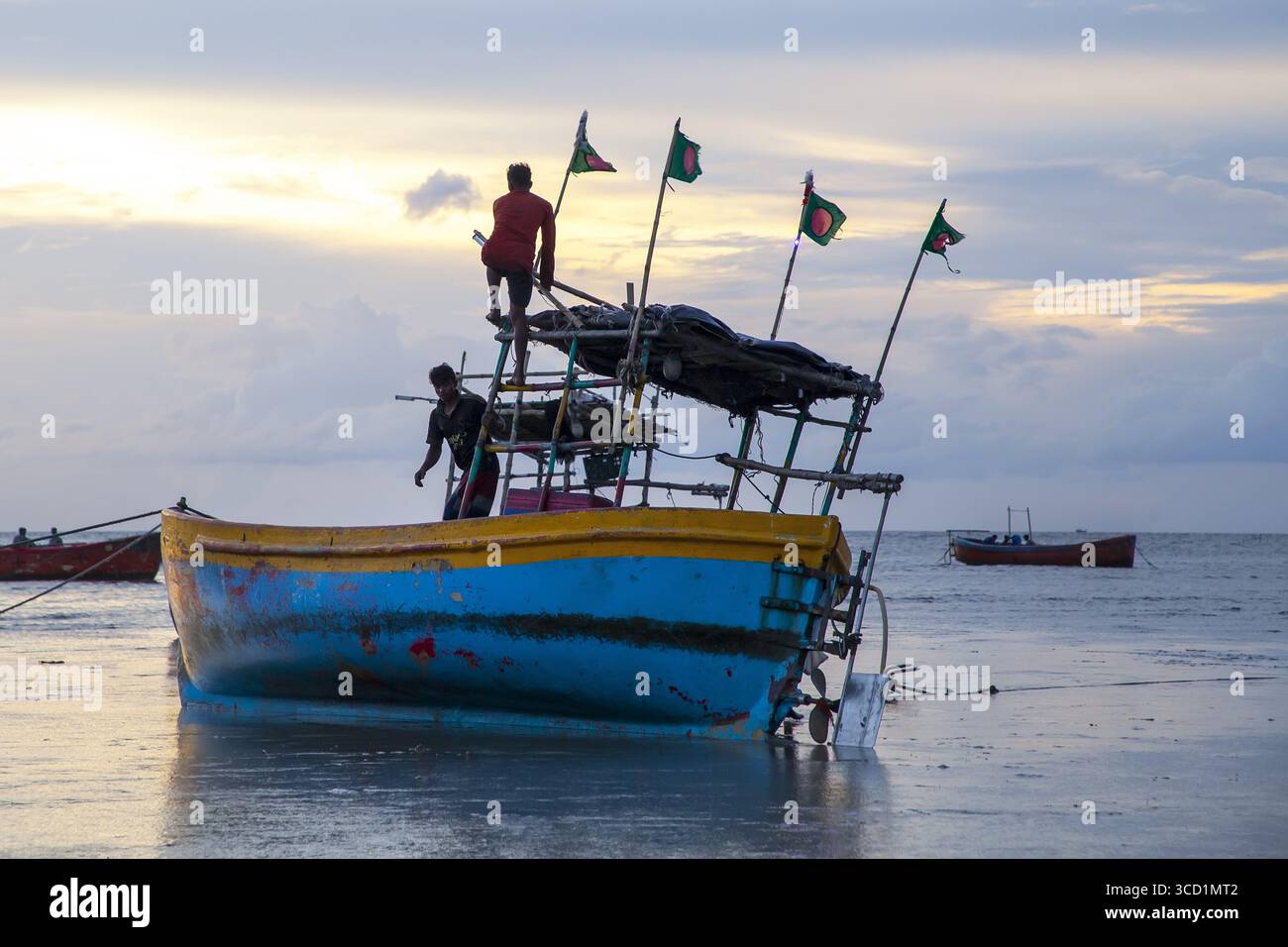 Chattogram, Bangladesh - 19 septembre 2023 : vue d'un bateau de pêche altéré orné de drapeaux bangladais, coincé sur une côte boueuse chatoyante, sous un ciel pastel. Banque D'Images