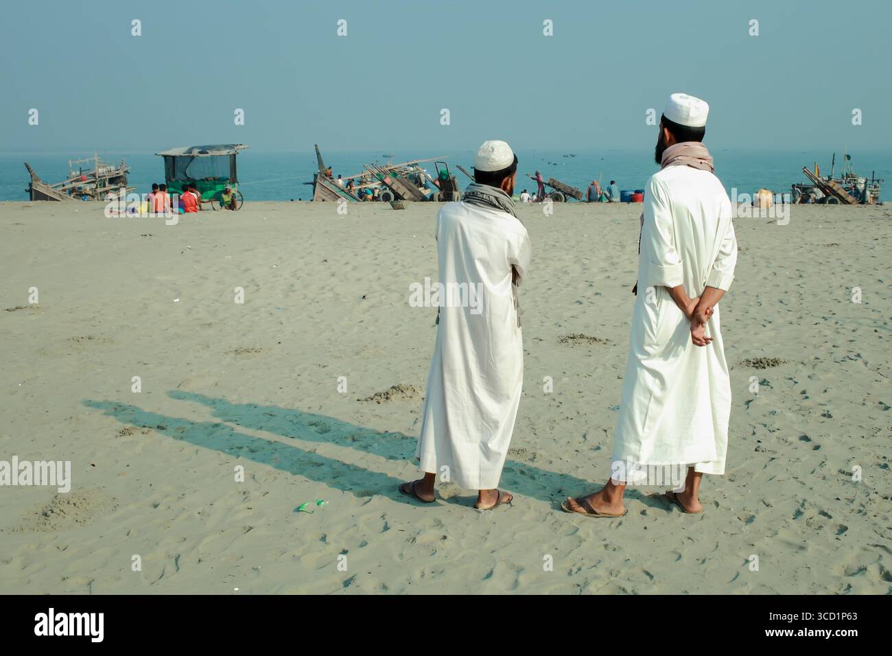 Cox's Bazar, Bangladesh - 07 mars 2022 : vue de deux personnages debout sur la plage de sable, regardant vers les bateaux de pêche lointains et le soleil serein Banque D'Images