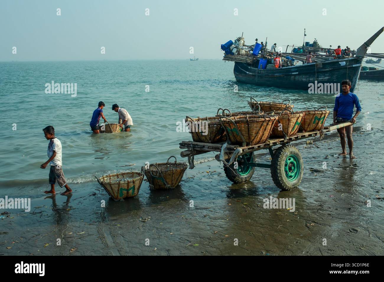 Cox's Bazar, Bangladesh - 07 mars 2022 : vue de pêcheurs transportant leurs prises à terre, contrastant avec le bois sombre et altéré du bateau de pêche Banque D'Images