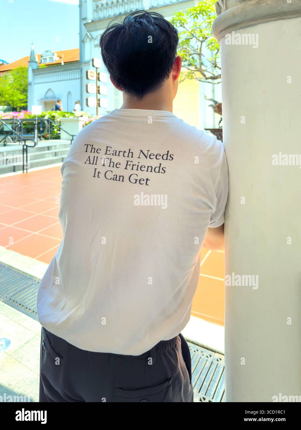 Un jeune asiatique se tient dehors avec un T-shirt qui dit « la Terre a besoin de tous les amis qu'elle peut obtenir », promouvant la sensibilisation à l'environnement Singapour Banque D'Images