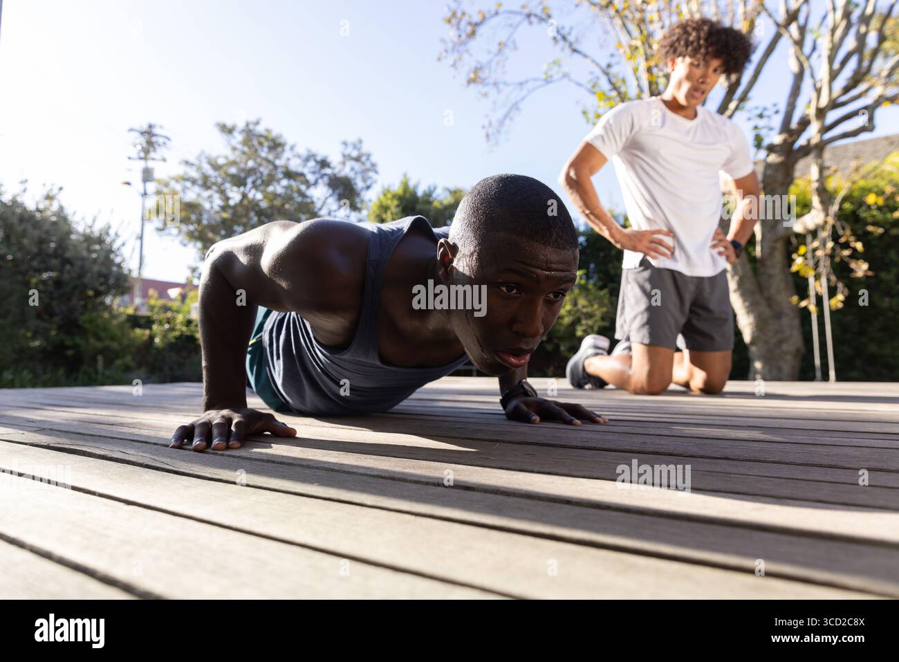 Entraîneur masculin diversifié guidant le stagiaire effectuant des pompes sur le pont en bois à l'extérieur avec smartwatch Banque D'Images