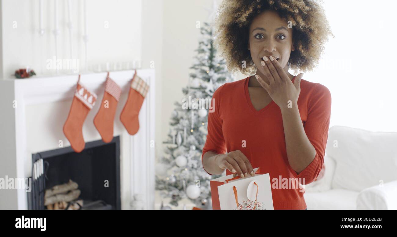 Jeune femme étonnée tenant un sac cadeau de Noël dans sa main regardant les yeux larges vers la caméra avec sa main à sa bouche Banque D'Images