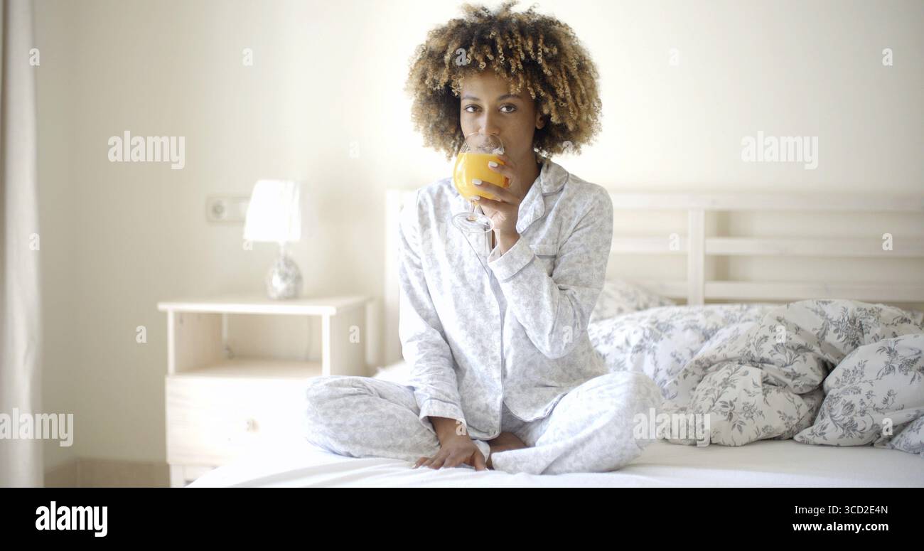 Heureuse fille noire buvant du jus frais sur le lit Banque D'Images
