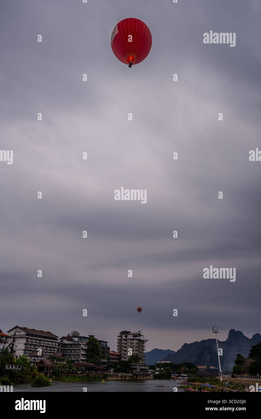Montgolfières flottant au-dessus de la rivière Nam Song et du paysage de montagne à Vang Vieng, Laos le jour nuageux avec Riverside Hotels in View Banque D'Images