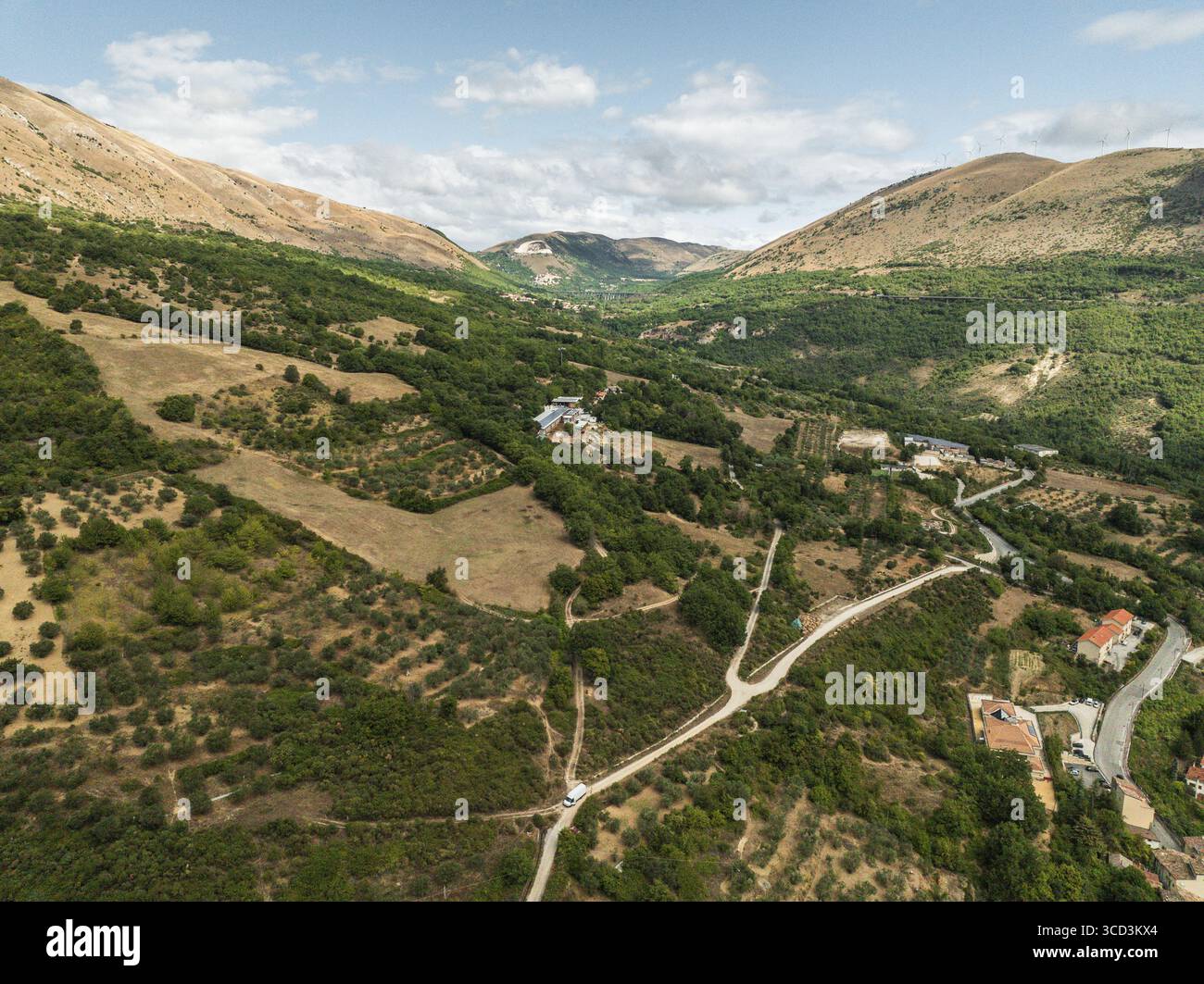 Vue aérienne des montagnes baignées de soleil en cascade dans la vallée, où une route sinueuse relie de petits groupes de bâtiments nichés dans une végétation luxuriante, Anversa degli Abruzzi, Abruzzes, Italie. Banque D'Images