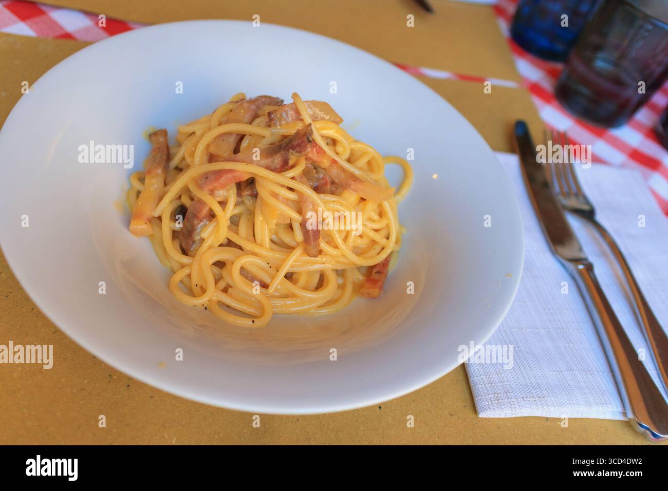 Une assiette de pâtes traditionnelles carbonara servie dans un confortable restaurant italien à Vérone. Les convives savourent les saveurs riches du plat dans un cadre chaleureux et accueillant Banque D'Images