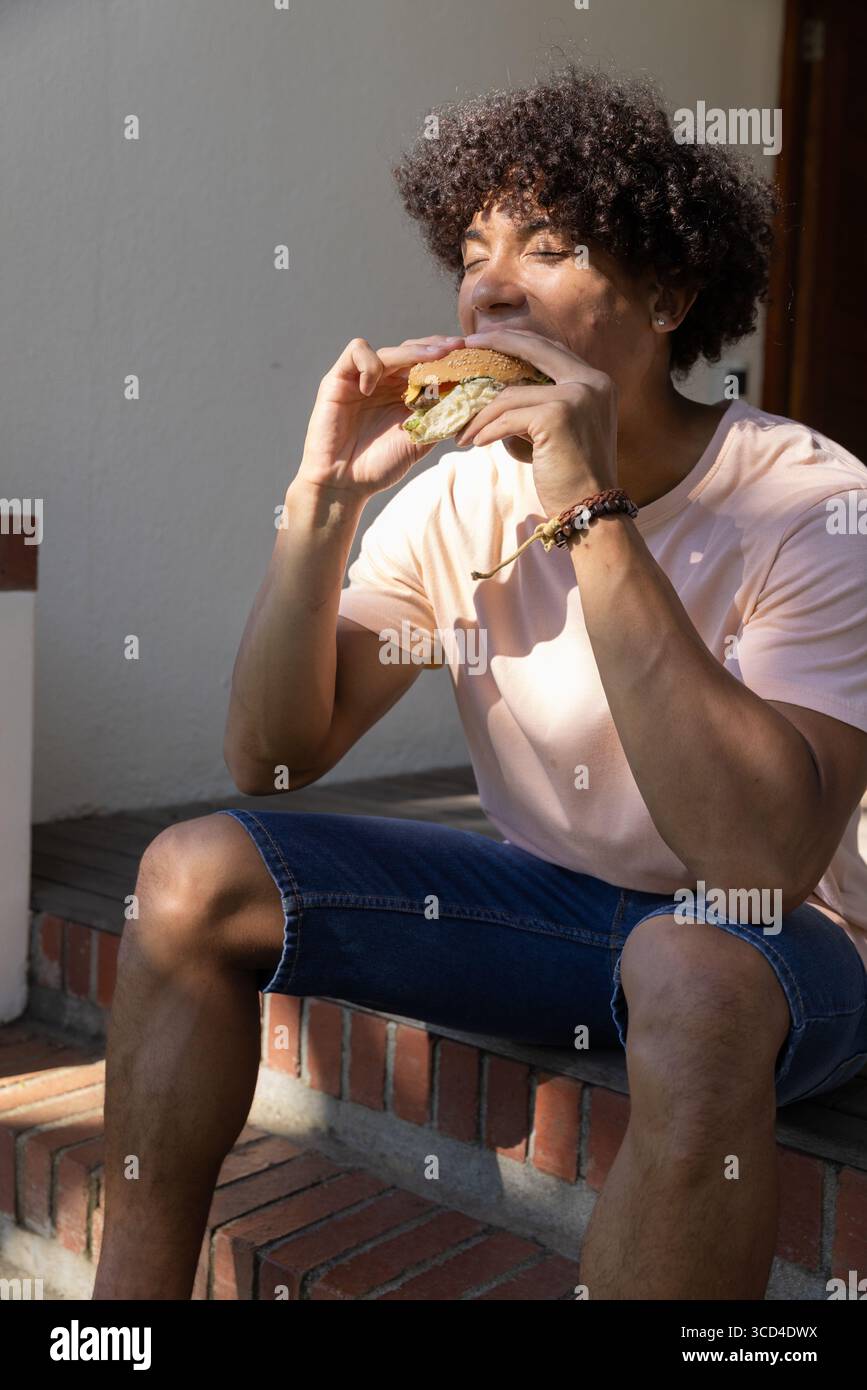Hamburger mordu sur des marches de briques ensoleillées au porche avant avec des bracelets perlés et un mur en stuc Banque D'Images
